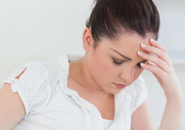 Woman wearing a white blouse holding her forehead